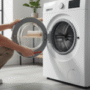 Photorealistic professional lifestyle photograph of a modern front-loading washing machine in a clean home laundry room, with a person's hands demonstrating the step-by-step process to open the door using the emergency release lever. Door slightly ajar revealing the interior drum, detailed textures on stainless steel and white enamel surfaces, natural daylight from window, high-resolution 8K, sharp focus, product photography quality, realistic shadows and reflections, 2024 model.